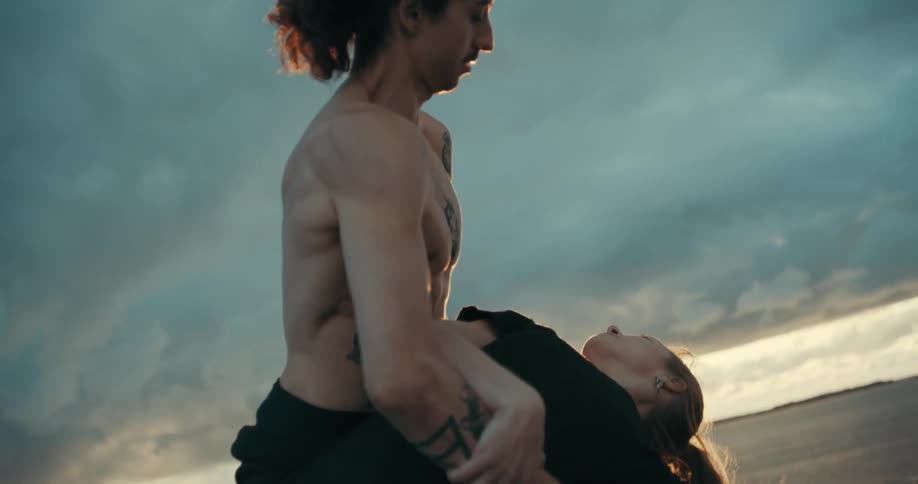 Young couple dancing ballet over a wooden pier next to the ocean at sunset