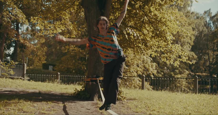 A man standing on a strap stretched between trees uses his arms to maintain balance