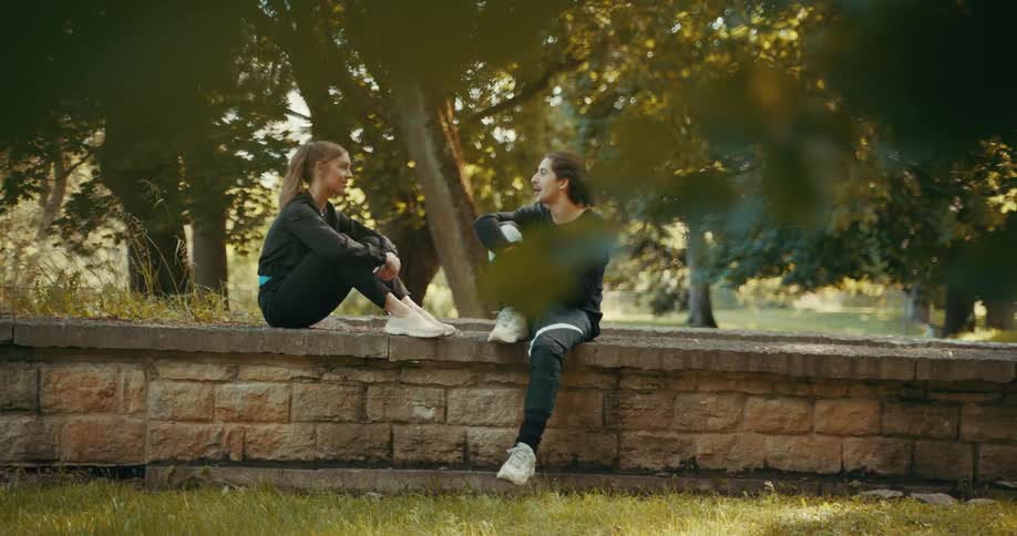 A woman and man chat together while sitting on a low stone wall outdoors during the day