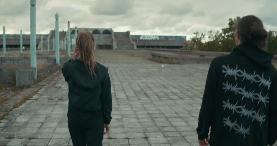 A young woman and man are walking on a brick road as he puts down his hood and birds fly overhead