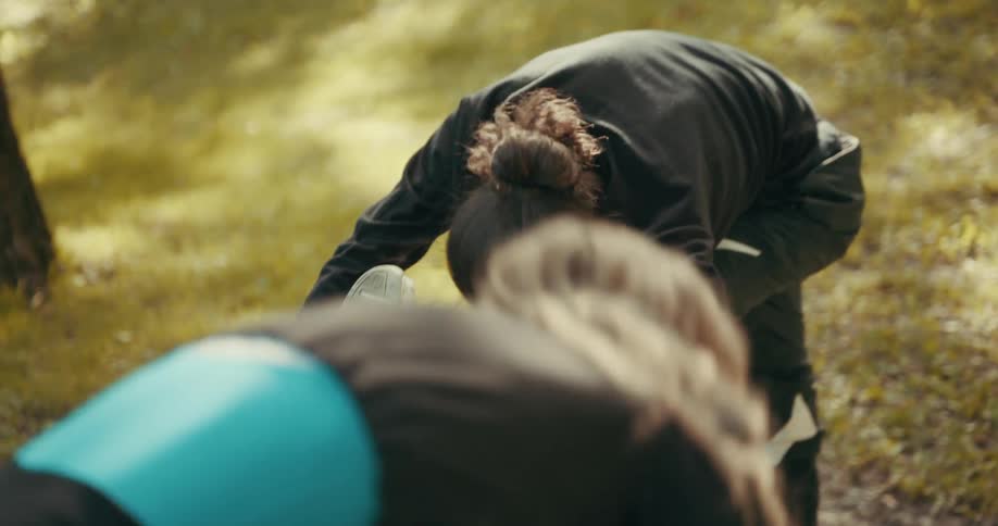A man is outside in a park holding on to a concrete block and doing stretching exercises with a woman