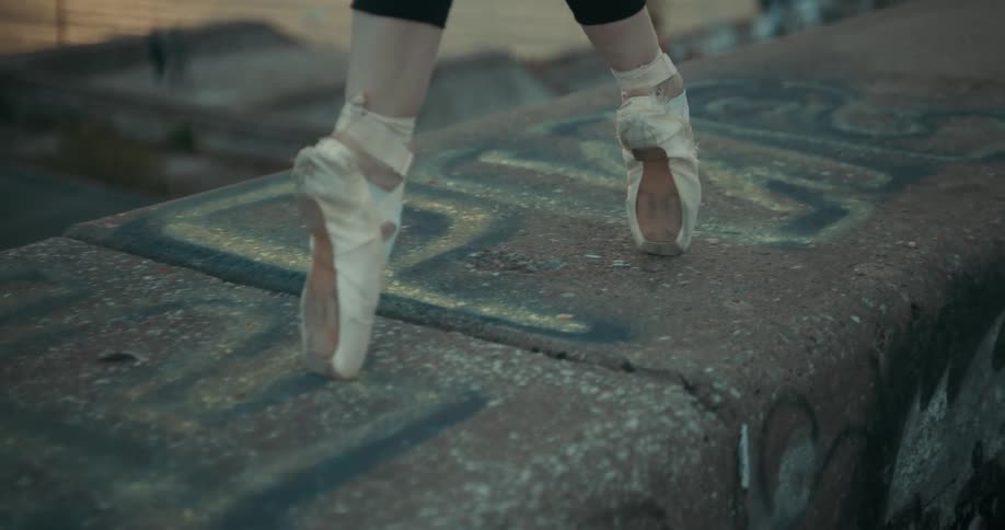 A ballet dancer walks en pointe along a cement ledge