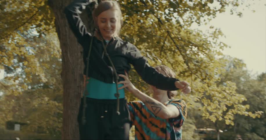 Man helps a woman to learn how to balance hanging from a rope in the backyard