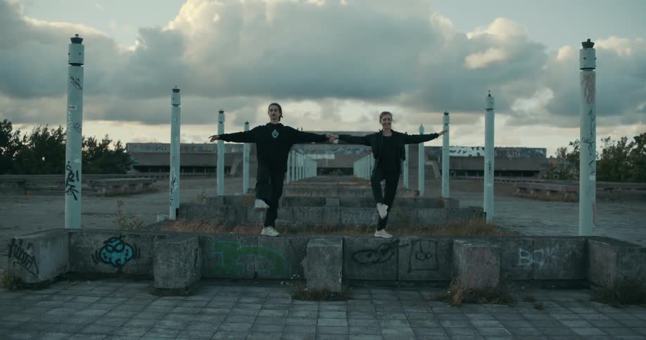 A man and a woman are outside standing on a cement wall as they practice their dance moves together