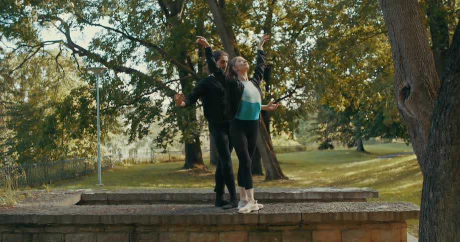 A man and a woman are outside standing on a cement wall in a park as they practice their dance moves together