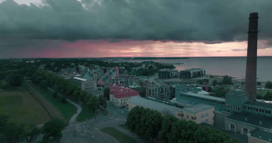 Factory and other buildings sit near shore under a red horizon and an overcast sky