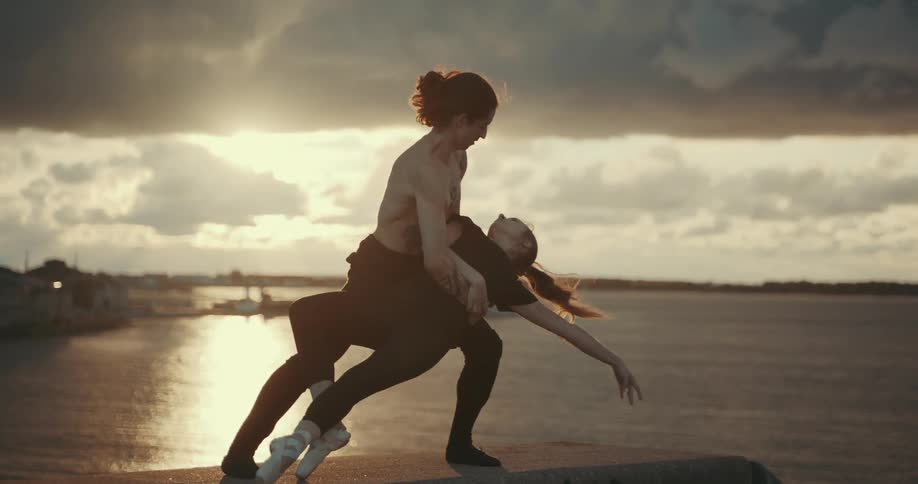 A young man on the shore holds on to a woman and wraps his arms around her as he dips her in a dance pose