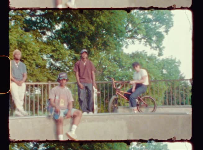Two teenage boys lean on a railing outside with another boy in front of them