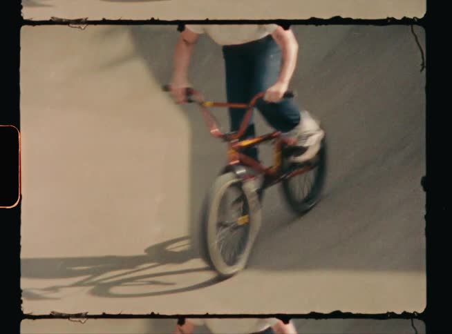 A teenage boy is riding his bike around in a concrete bowl at a skateboard park