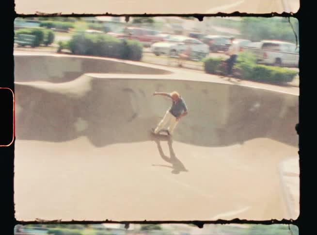 Skateboarder skates around skate park concrete bowl as others watch
