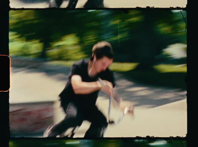A man in a skate park hops with his bicycle to grind across a ledge with his wheel pegs