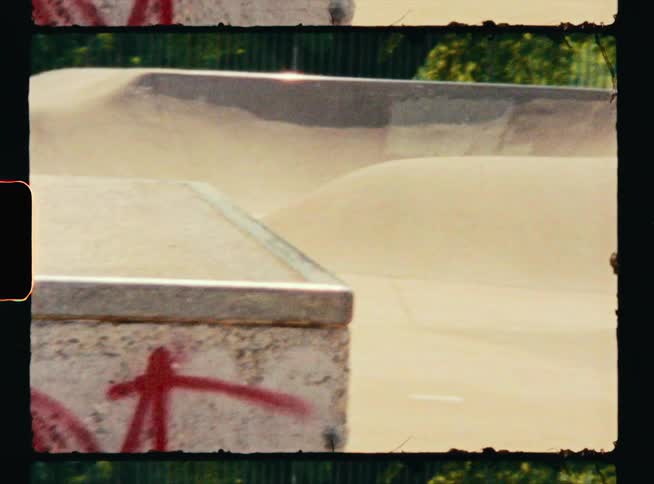 A teenage boy is riding his skateboard at a skateboard park and he goes over a ramp and leaps up to the cement block