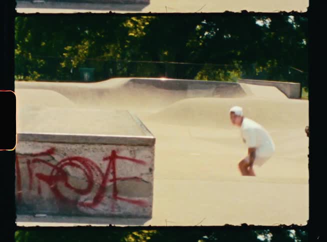 Vintage footage of a teenage boy skateboarding up a ramp and across a ledge at a skateboard park
