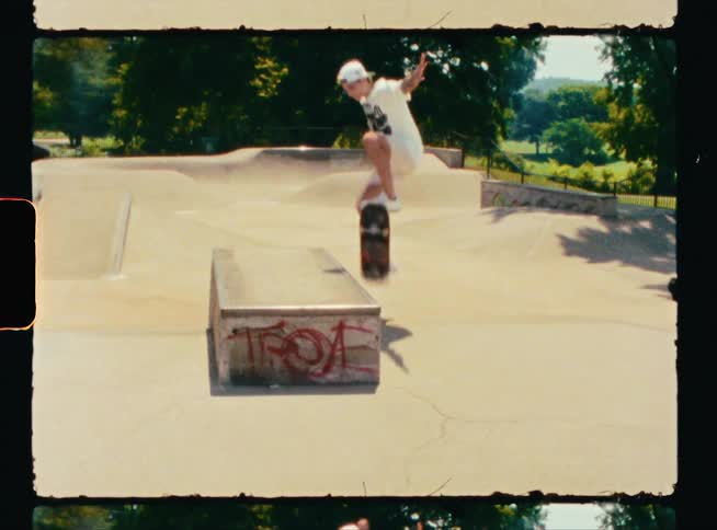 A teenage boy is riding his skateboard at a skateboard park and he goes over a ramp and leaps up to the cement block above