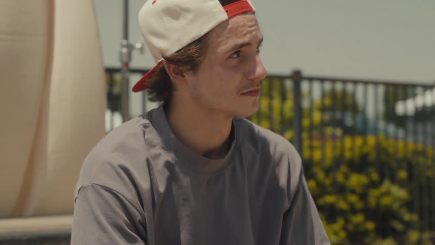 A teenage boy sits at a park and looks in to the distance