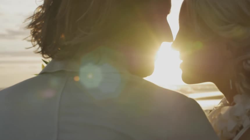 A man and woman kiss on the beach at sunset