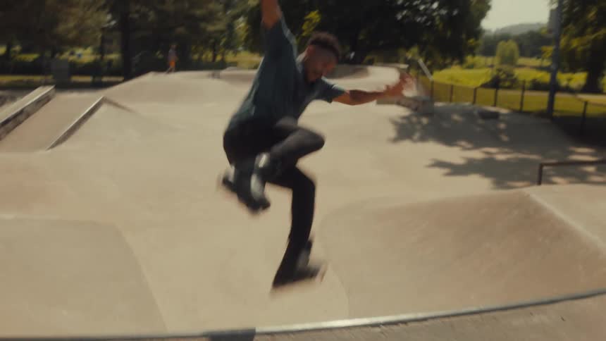 A teenage boy on skates leaps over the edge of a concrete bowl in a skate park