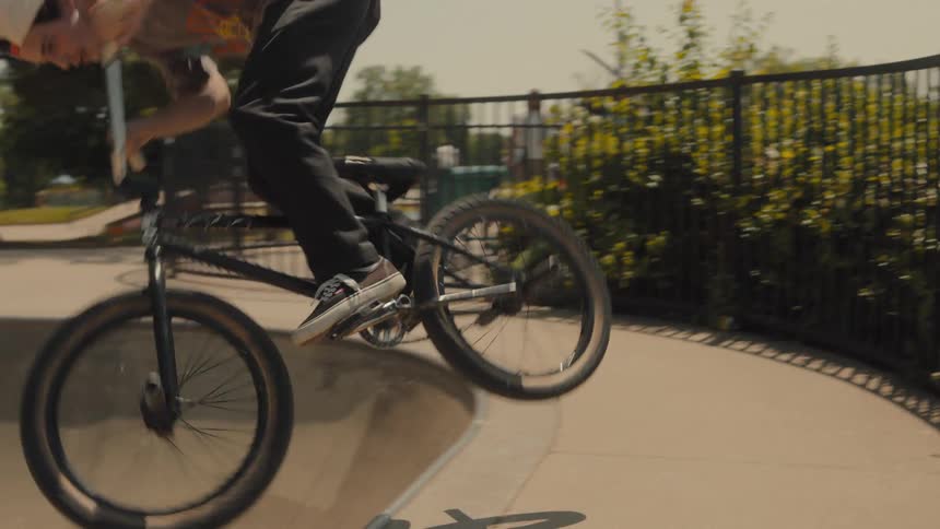 Youth rides bike down sloping concrete bowl in skate park