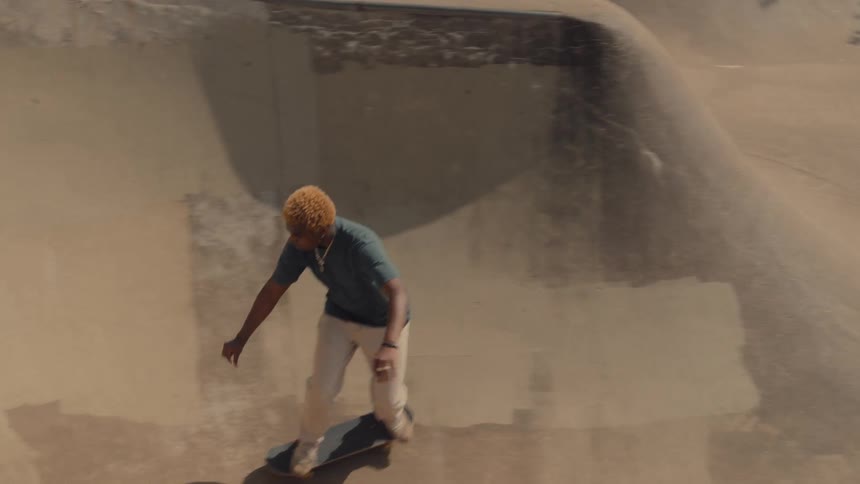 A young black man is skate boarding outside in the summer time