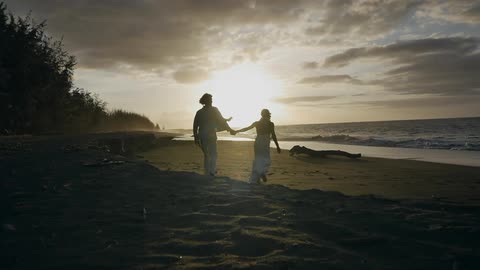 A couple holding hands while walking along the beach at sunset