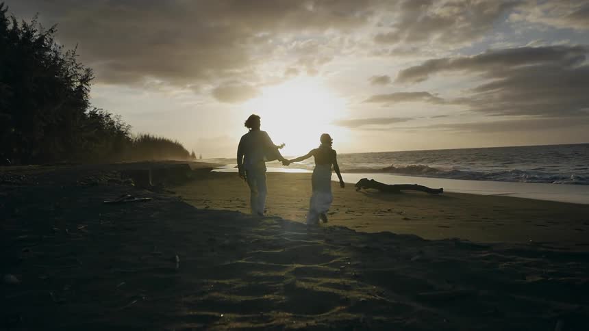 A couple holding hands while walking along the beach at sunset