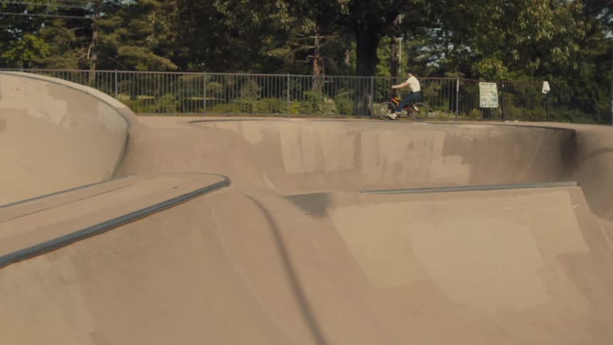 Two young men watch as a friend rides his bike along the edge of the skate park bowl
