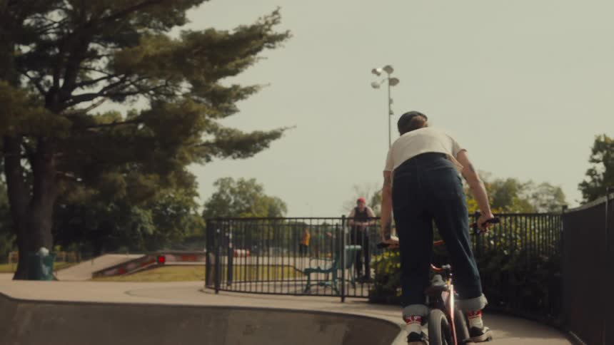 Woman rides bike down slope into skate park concrete bowl
