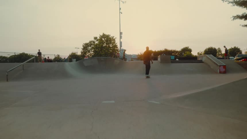 A teenage boy skateboards up a ramp at a skateboard park and walks towards his friends