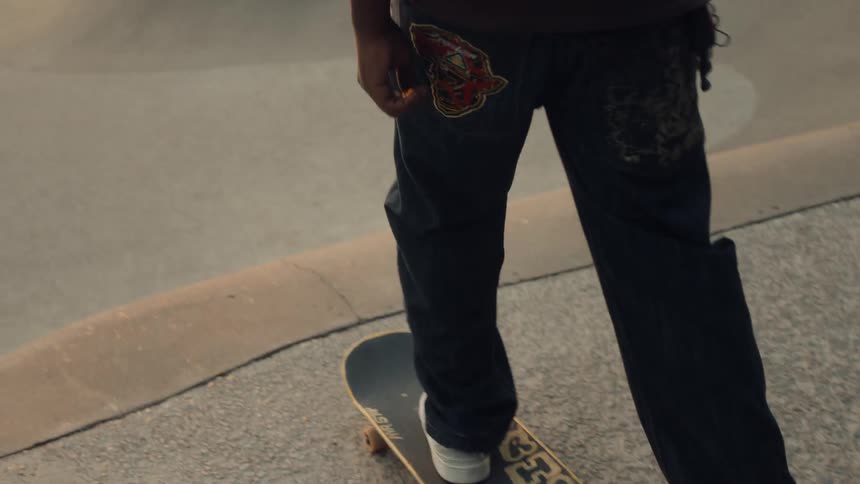 The sun hangs low in the sky as a young man prepares to skate down ramp at a skate park