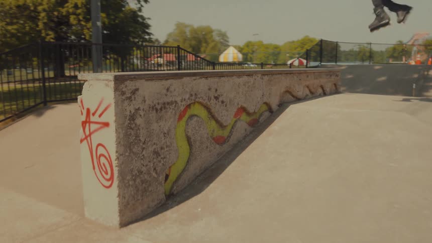 A teenage boy on rollerblades leaps over a concrete ramp at a skate park and twists in the air