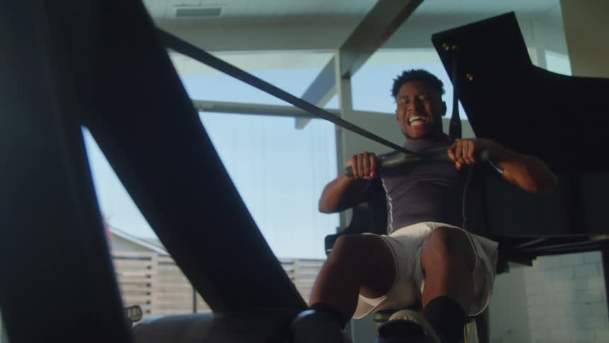 A man scowls while exercising on a rowing machine indoors during the day