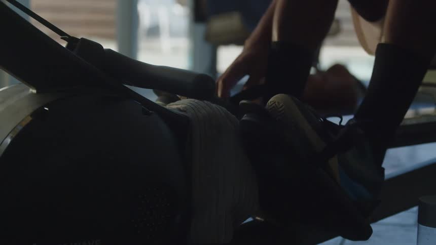 A man straps his feet into the rowing machine before starting his workout
