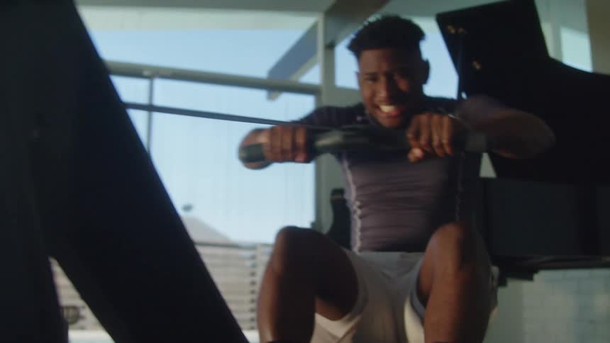 A man grimaces and strains as he works out on a rowing machine at home