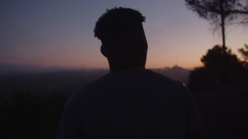 The silhouette of a man standing outside swaying as he looks out at the sunset