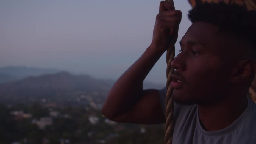 A man is holding on to a rope as he gently swings over the side of a mountain overlooking a city below