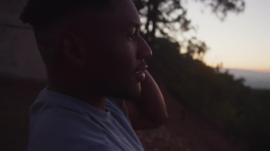 A man is sitting on a swing outdoors in nature during dusk