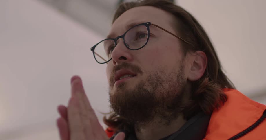 A man indoors rubs his hands together and blows on them and looks around the room