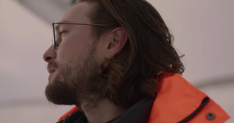 A man with a beard and wearing glasses is looking around outside
