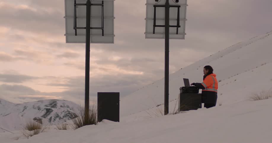 A man works on his laptop along the side of a snow covered hill