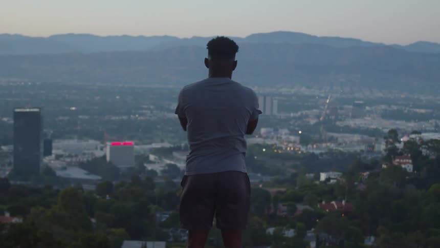 A man stretches his arms while standing on a hill overlooking a city