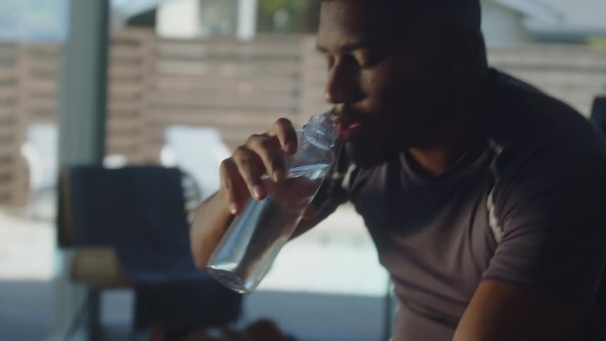 Man sitting near sliding glass doors with view of yard drinks water out of bottle