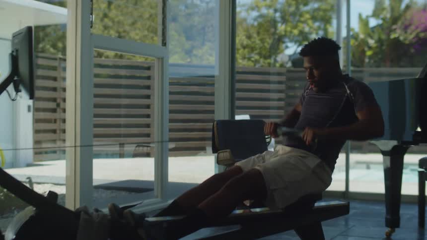 A man is exercising on a rowing machine in his house