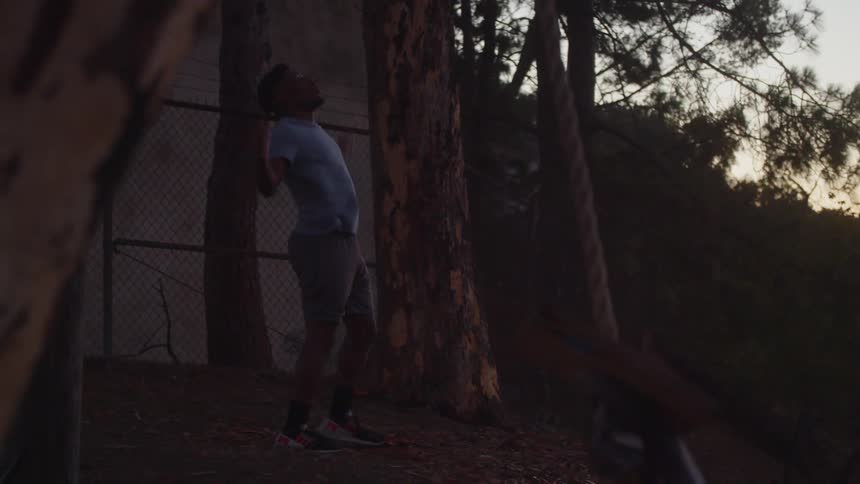 A man runs down a hill and raises his arms in the air as he stands near trees
