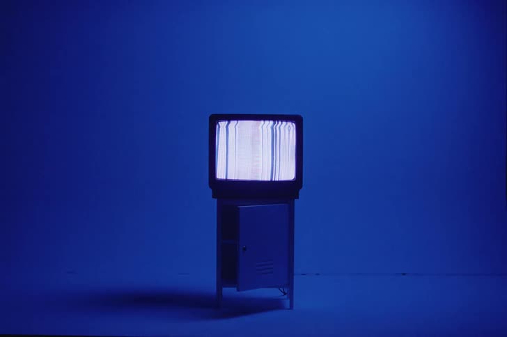 Colored blue lighting shifts over television and casts a shadow