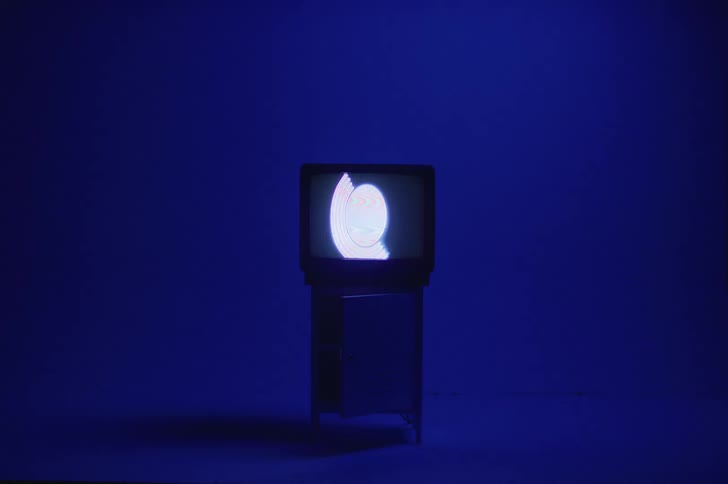 An image of a circle and arch play on a box style television in an empty room