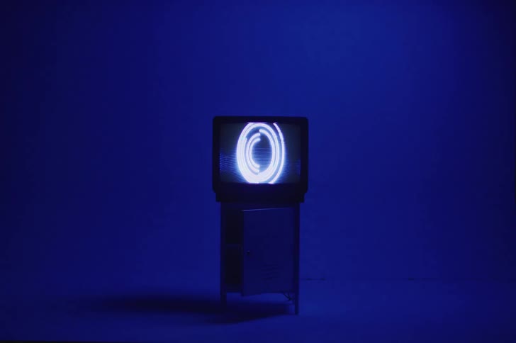 A circular pattern and designs move on a television screen sitting in a deep blue empty room