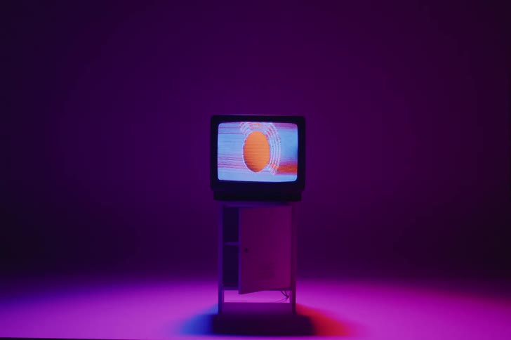 An older model television atop a small cabinet displays an strange image of an oval
