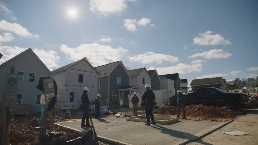 Construction workers wearing hardhats are standing outside in front a housing development they are building