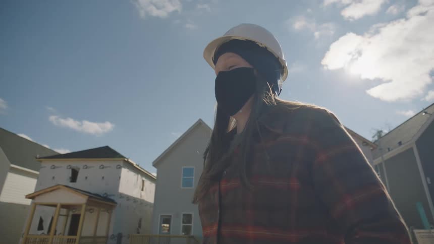 Two construction workers stand in front of houses being built