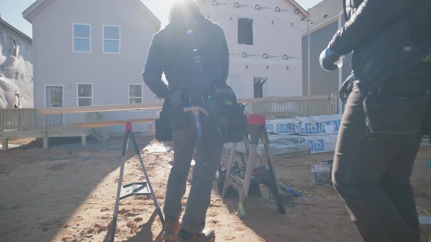 Two construction workers are standing outside in front a housing development they are building and checking their tool belts